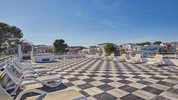 A checkered deck with lounge chairs, a railing, and buildings in the background.