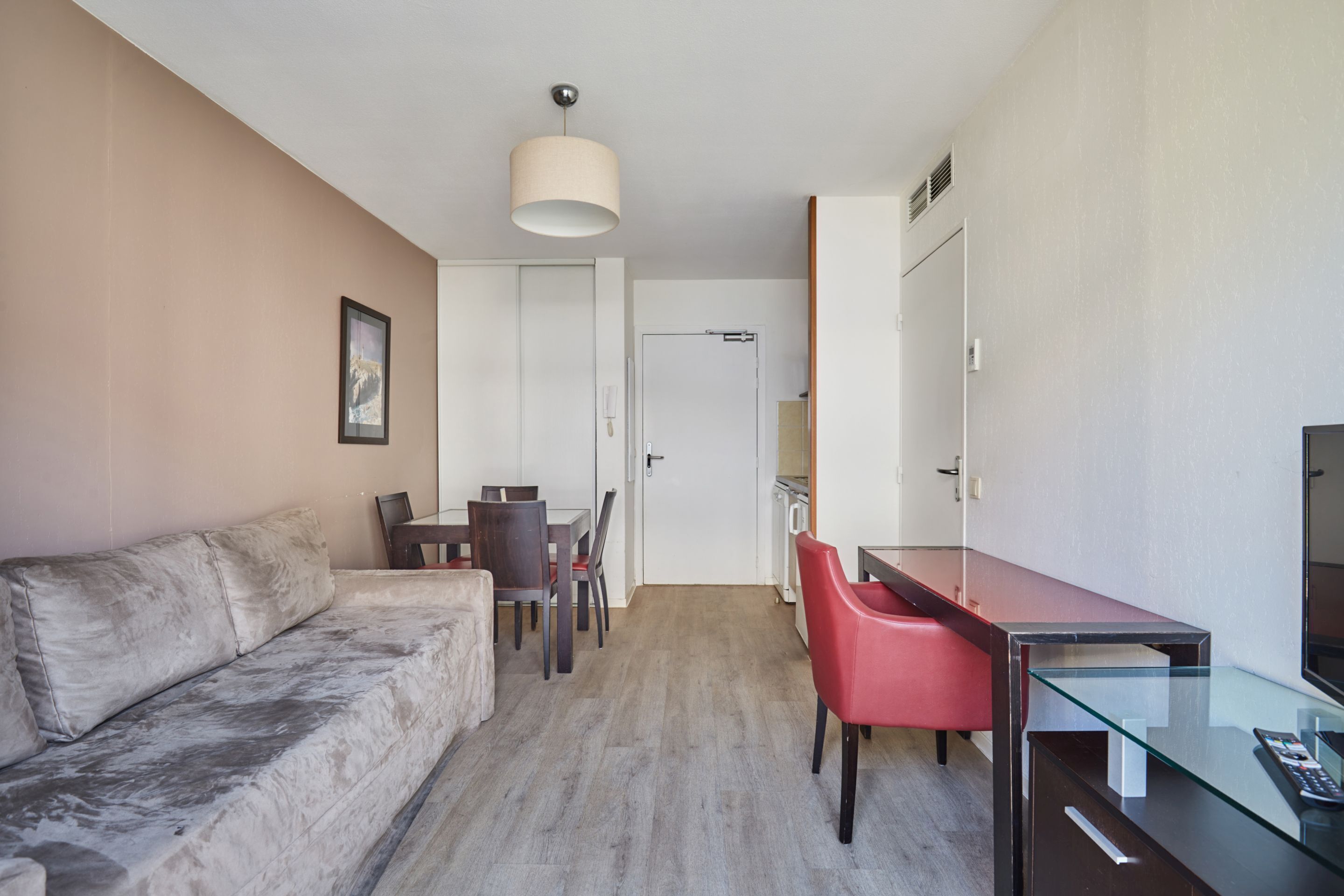A modern hotel room with a sofa, dining table, chairs, a desk with a computer, and a TV.