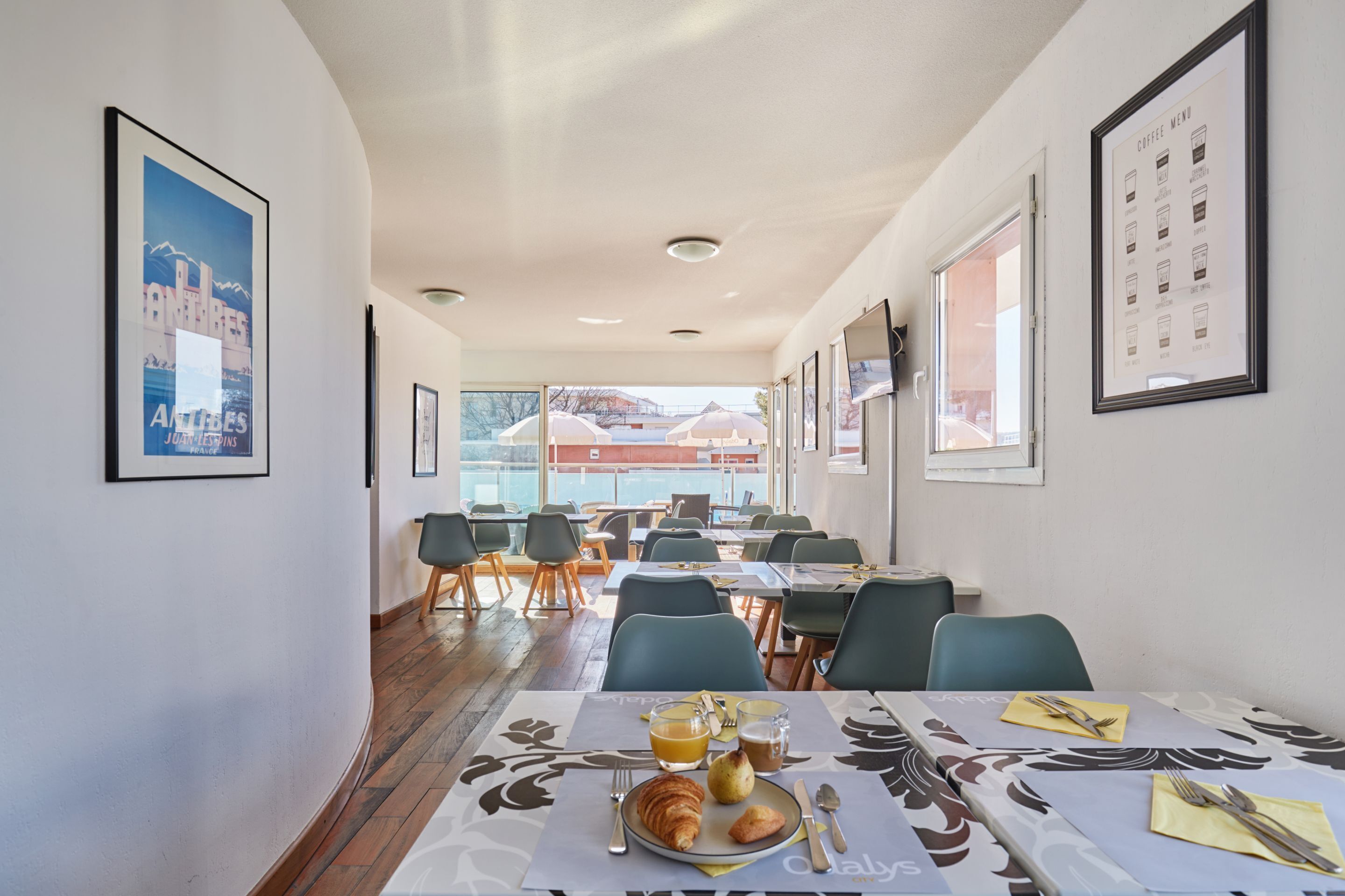 A dining area with tables set for breakfast, framed pictures on the walls, and a view of buildings outside.