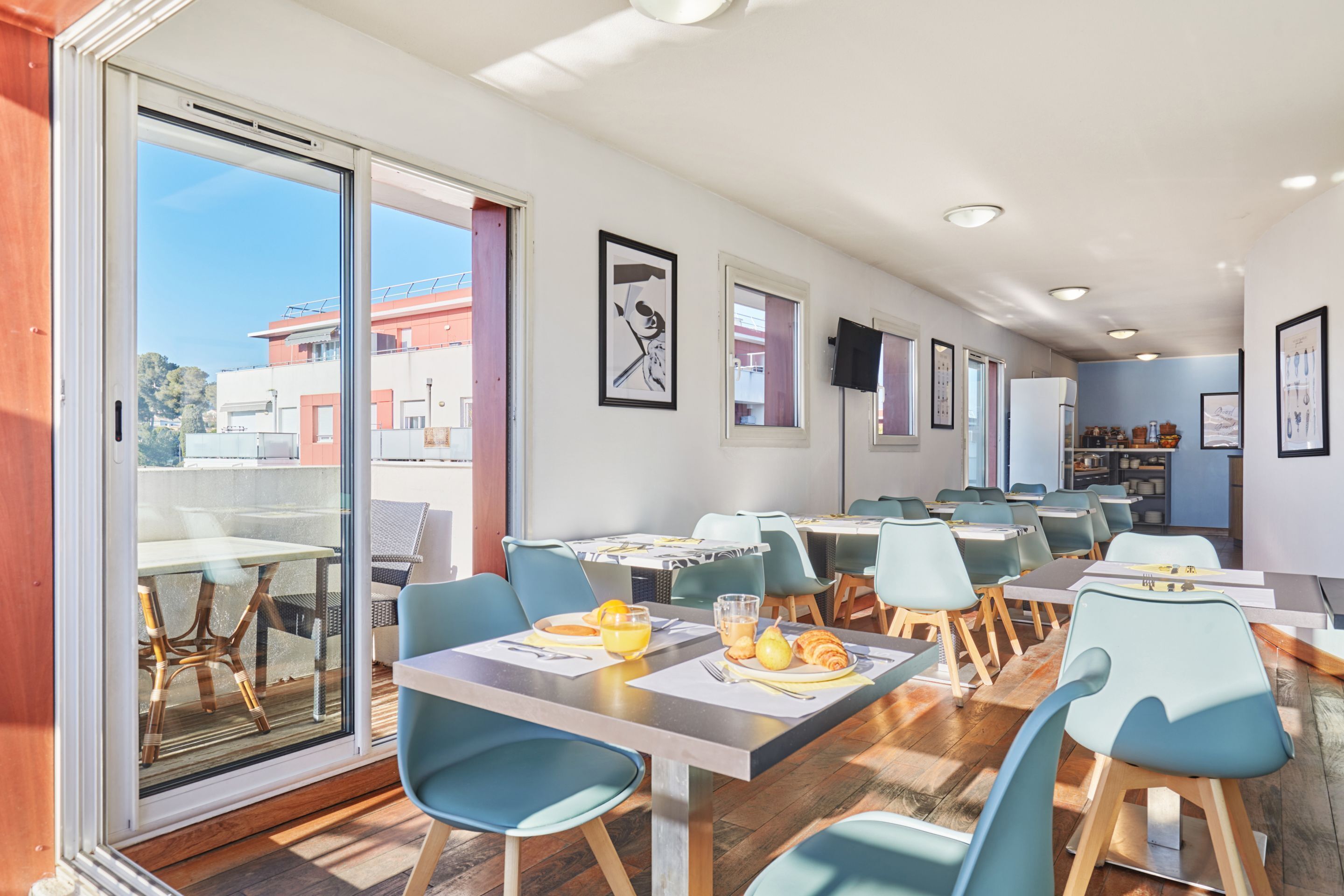 A dining area with tables and chairs, a view through a glass door, and framed artwork on the walls.