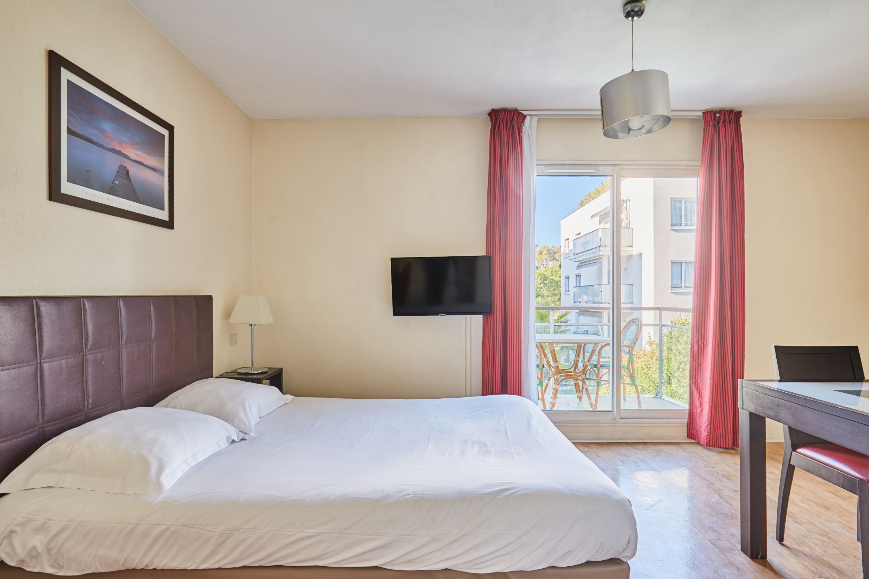 Una habitación de hotel con cama, televisor, escritorio y ventana con cortinas.