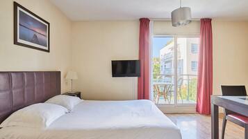 Una habitación de hotel con cama, televisor, escritorio y ventana con cortinas.