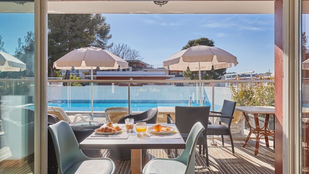 Un espace repas aménagé au bord de la piscine, avec des tables, des chaises et des parasols.