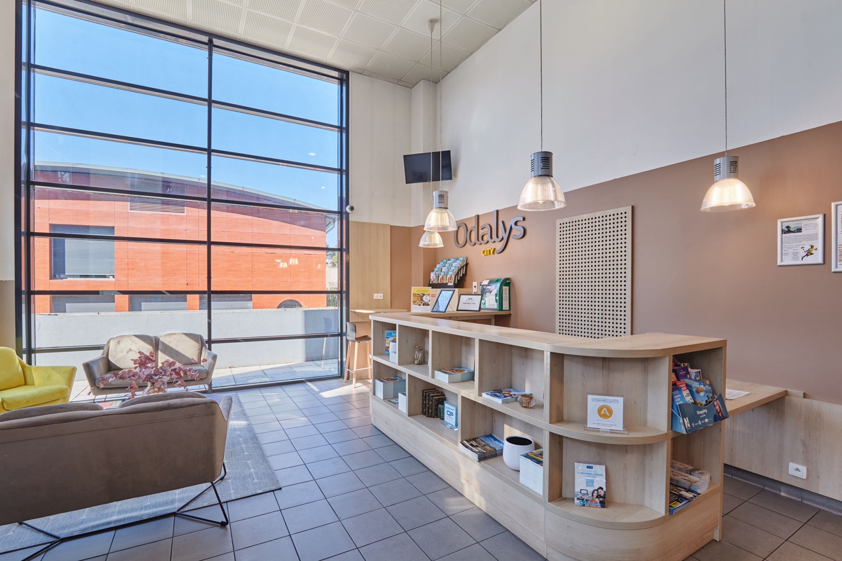 Un área de recepción con un escritorio de madera, estanterías con material informativo, un televisor y un amplio ventanal con vistas al exterior.