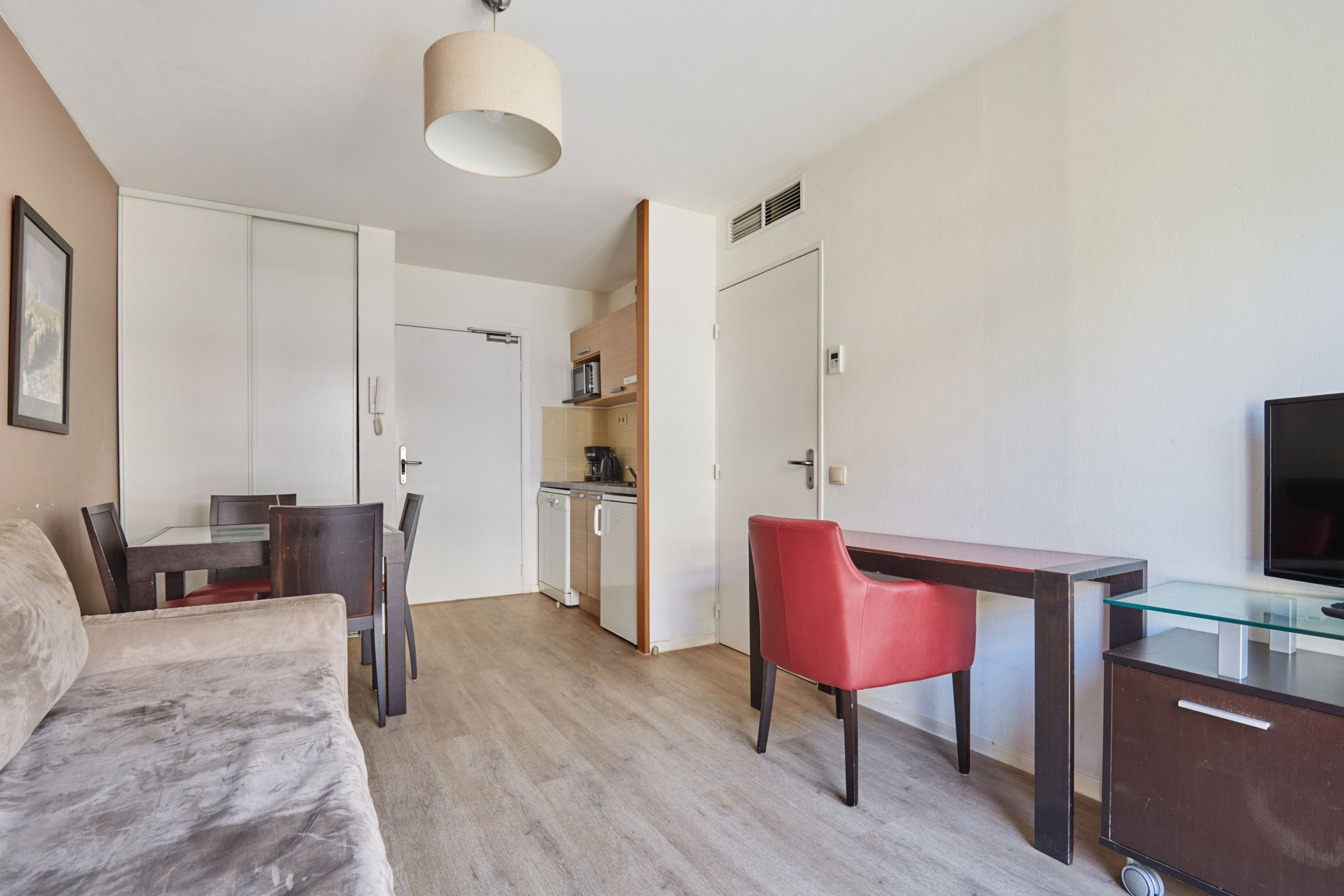 A modern hotel room with a bed, a desk with a chair, a TV, and a kitchenette.