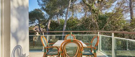 A balcony with a table and chairs, overlooking a natural landscape with trees and a clear sky.