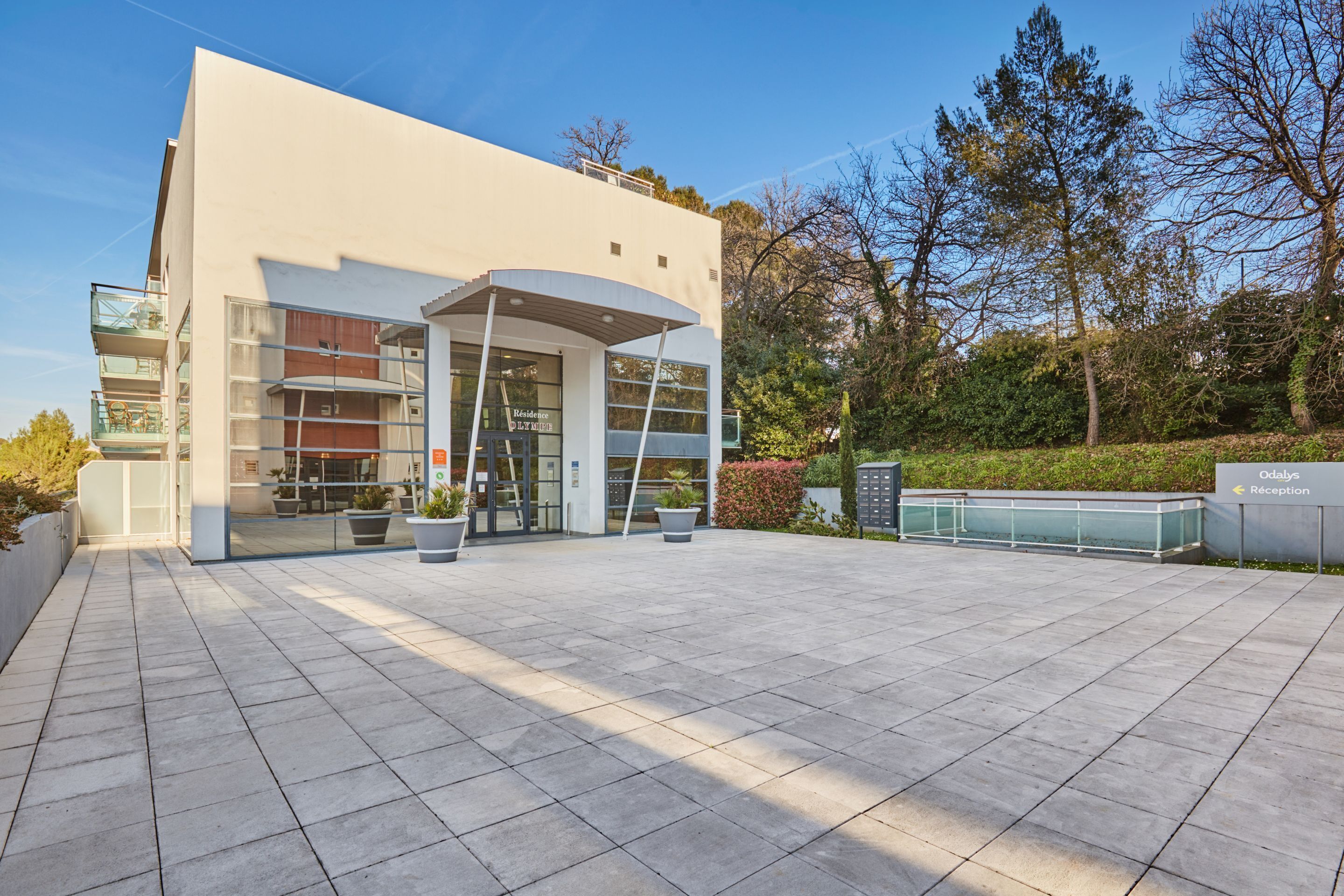 A modern building with a reception area, large windows, and a paved entrance.