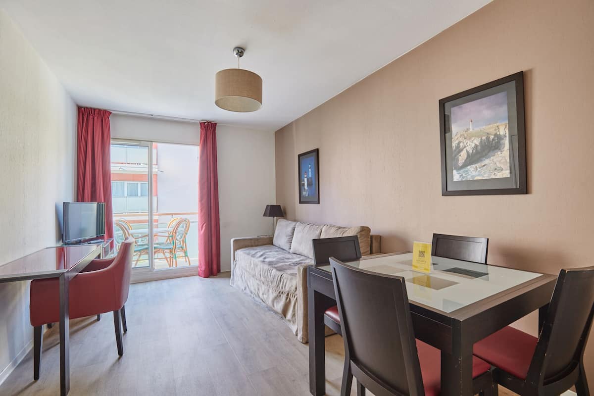 Ein Hotelzimmer mit Esstisch, Stühlen, einer Couch, einem Fernseher und einem Balkon mit Blick.