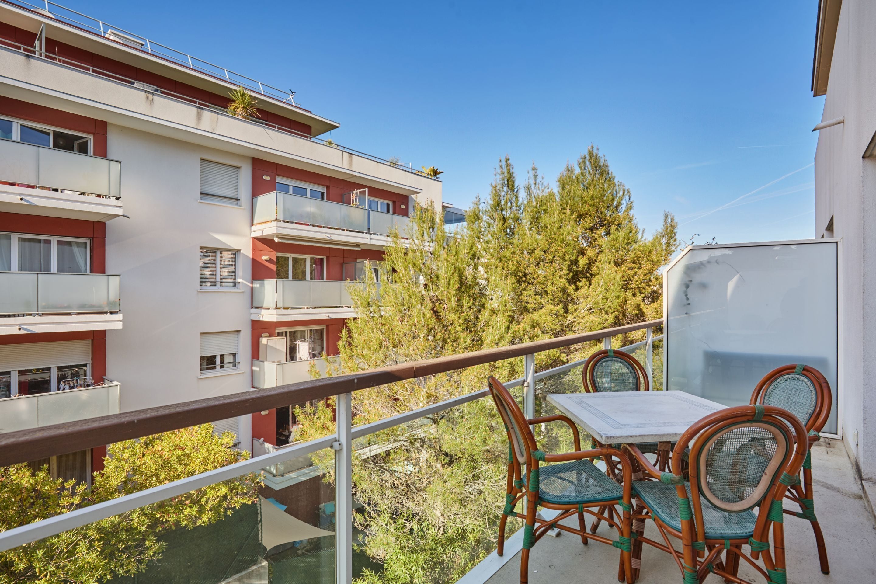 Un balcón con mesa y sillas, con vista a una zona residencial con edificios de varios pisos y árboles.