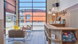 Un espace d’accueil doté d’une grande fenêtre, d’un comptoir de réception et d’un coin salon avec un fauteuil jaune.