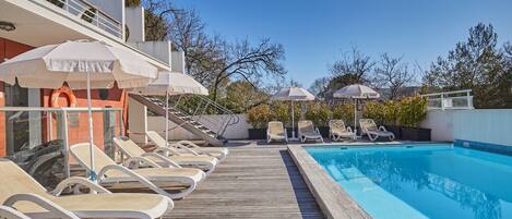 A poolside area with lounge chairs and umbrellas, a wooden deck, and a clear blue pool.