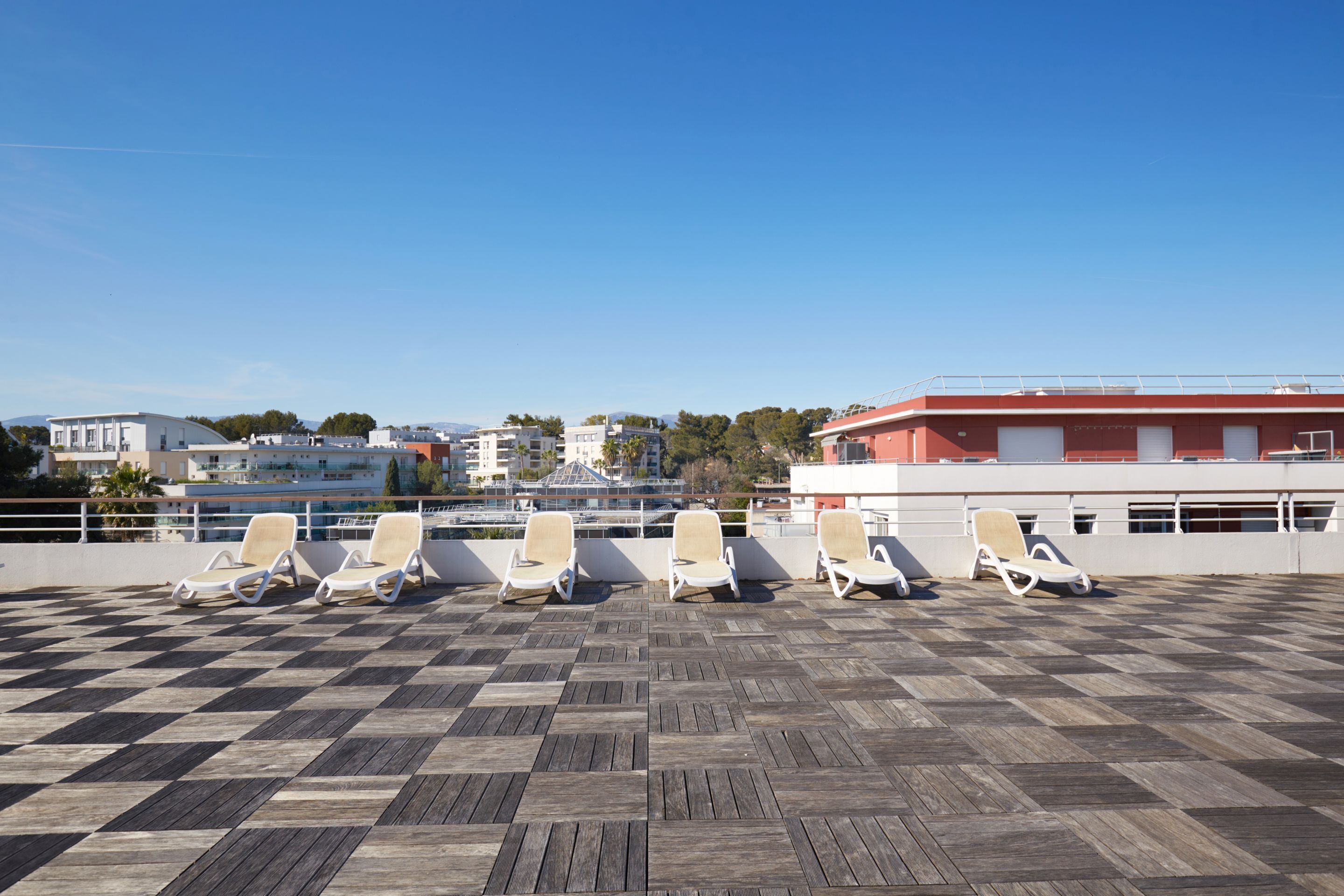 Een terras op het dak met een geruit vloerkleed en meerdere ligbedden.