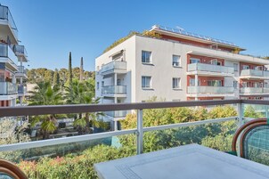 A modern apartment building with balconies, a terrace, and a view of greenery.