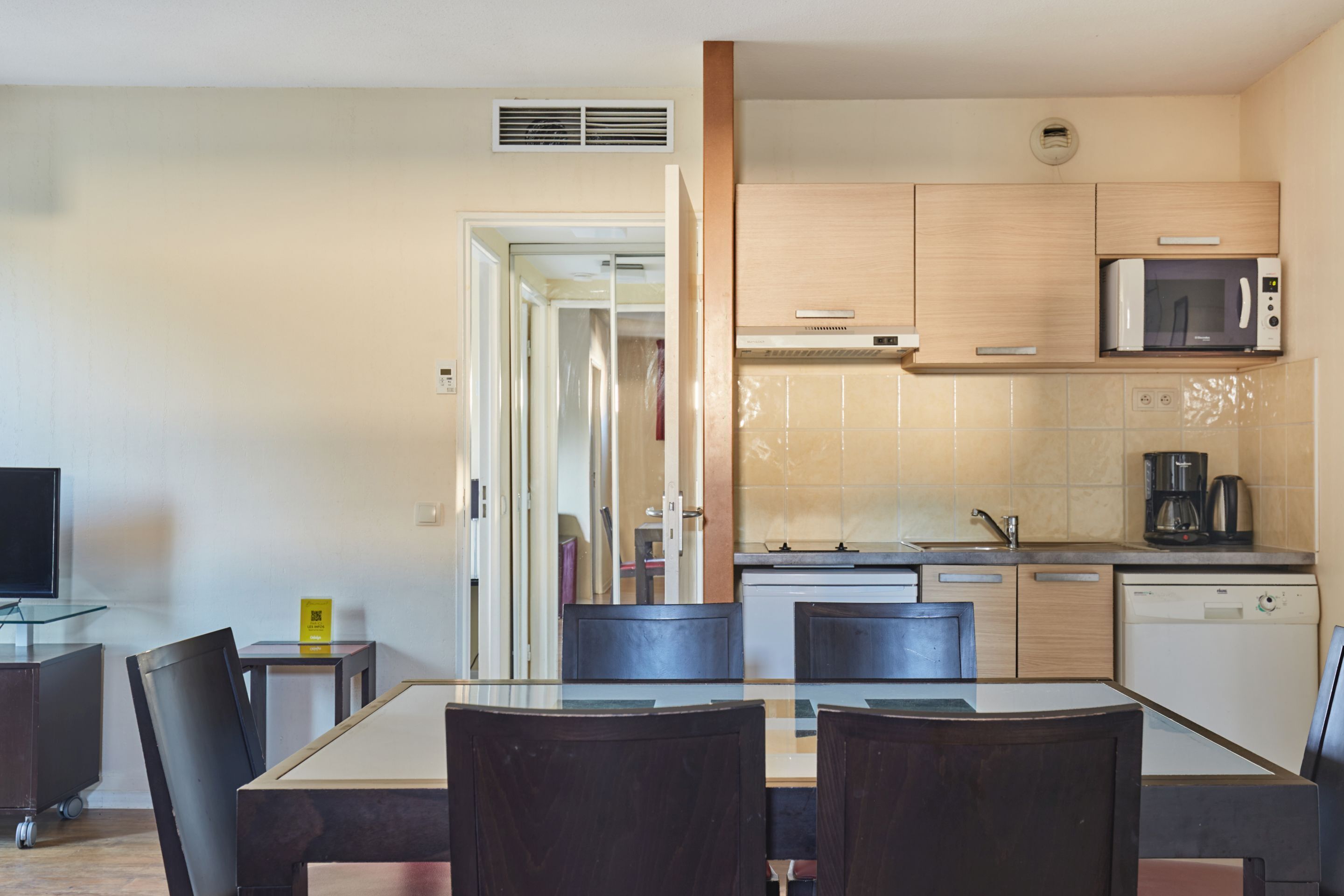 A compact kitchen with a microwave, coffee maker, and dishwasher. There is a dining area with a table and chairs.