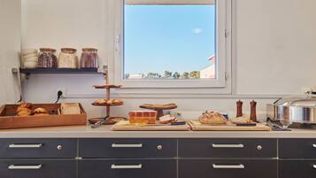 A kitchen with a window, jars on a shelf, a bread tray, and a cutting board with bread.