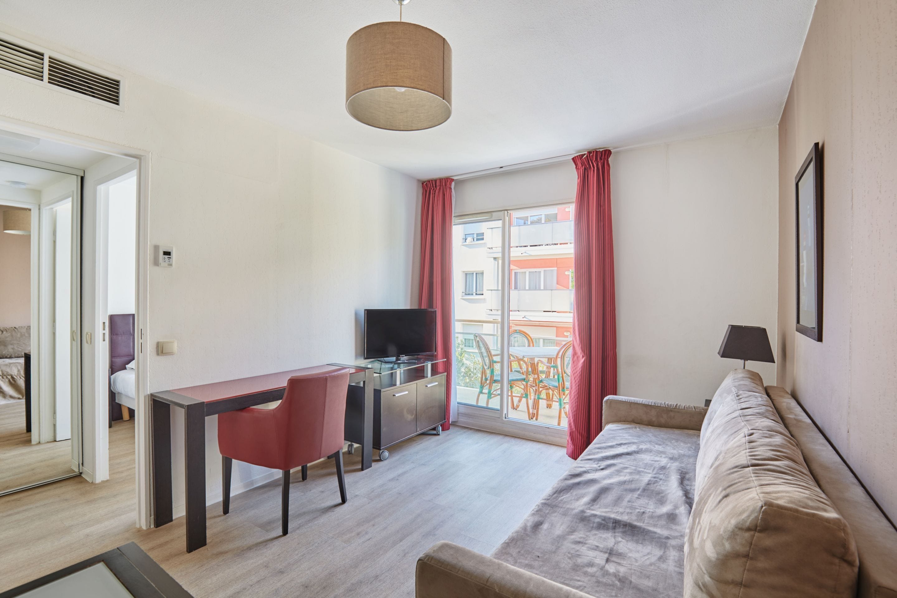 Una camera moderna con un letto, una scrivania con sedia, una TV e un balcone con tende rosse.