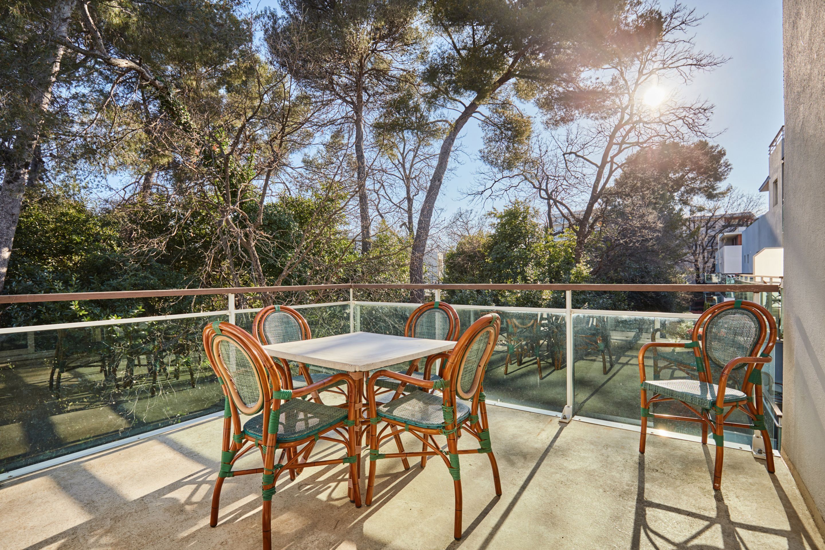 Un balcon avec une table et des chaises, donnant sur un jardin arboré et un ciel dégagé.