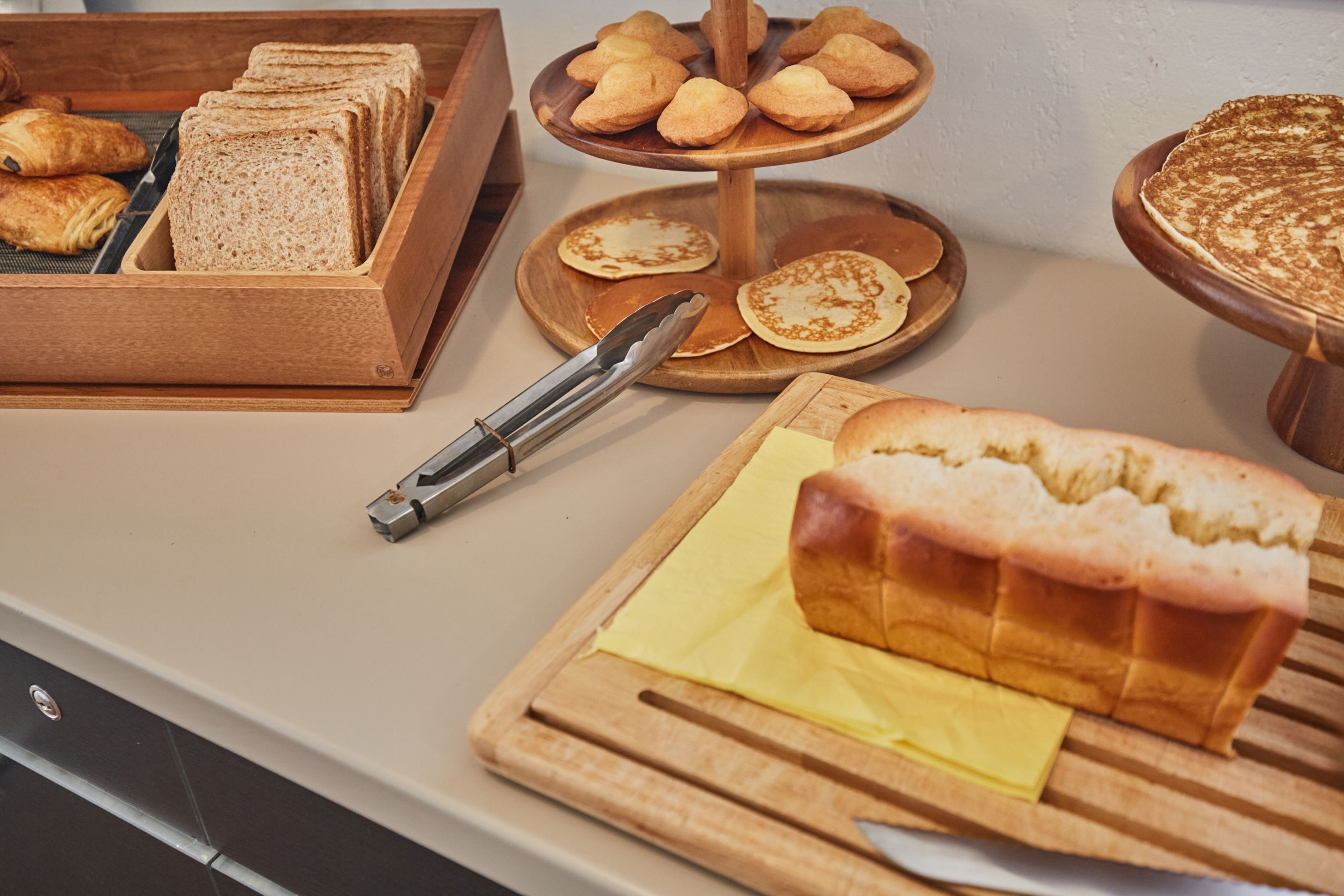 A breakfast buffet with bread, pastries, and a loaf of bread on a cutting board.