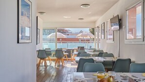 Un espace repas avec des tables, des chaises et une vue sur les bâtiments, grâce à de grandes fenêtres.