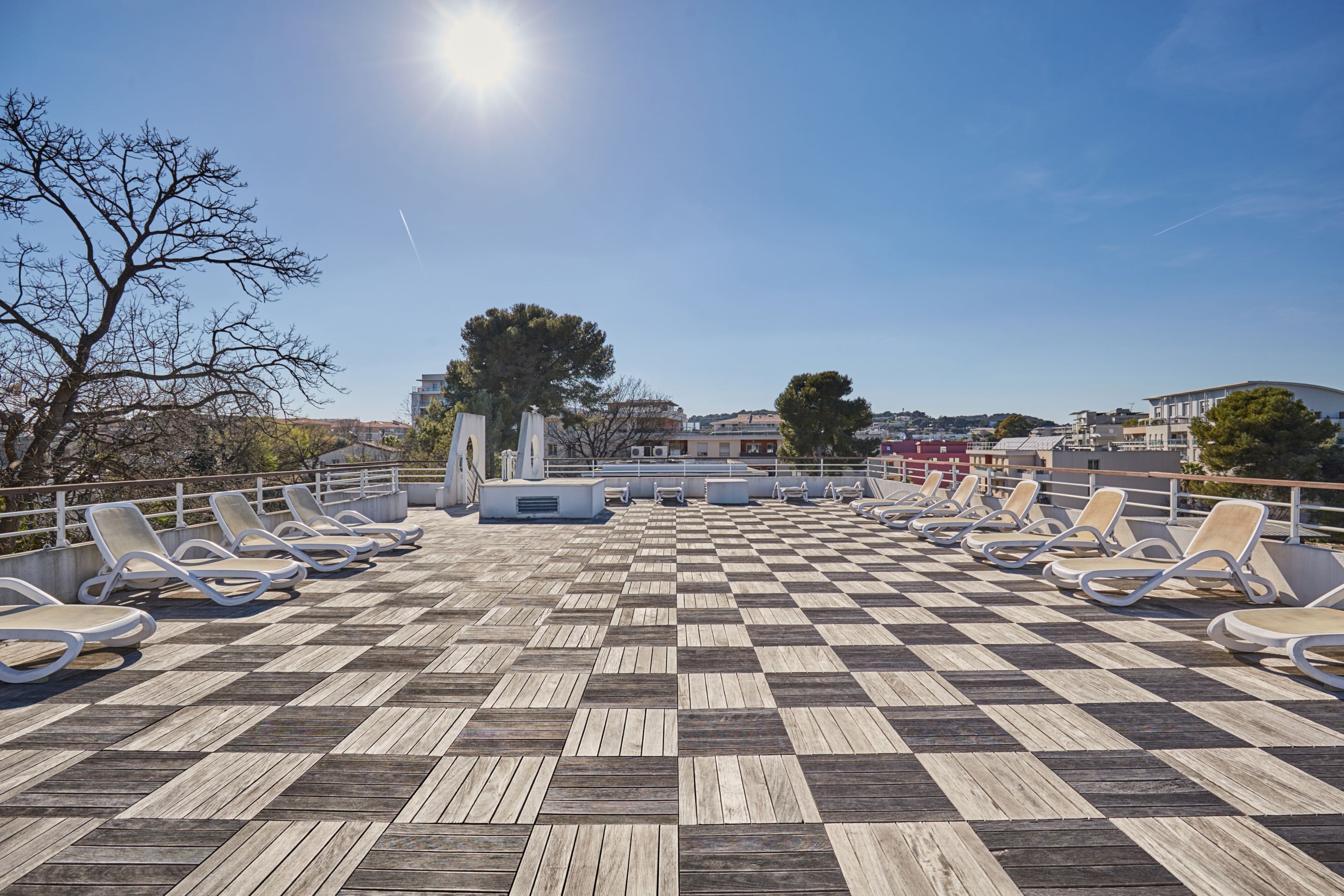 Eine sonnendurchflutete Terrasse mit Schachbrettmuster und Liegestühlen.