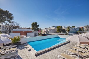 A rooftop swimming pool with lounge chairs and umbrellas, surrounded by buildings.