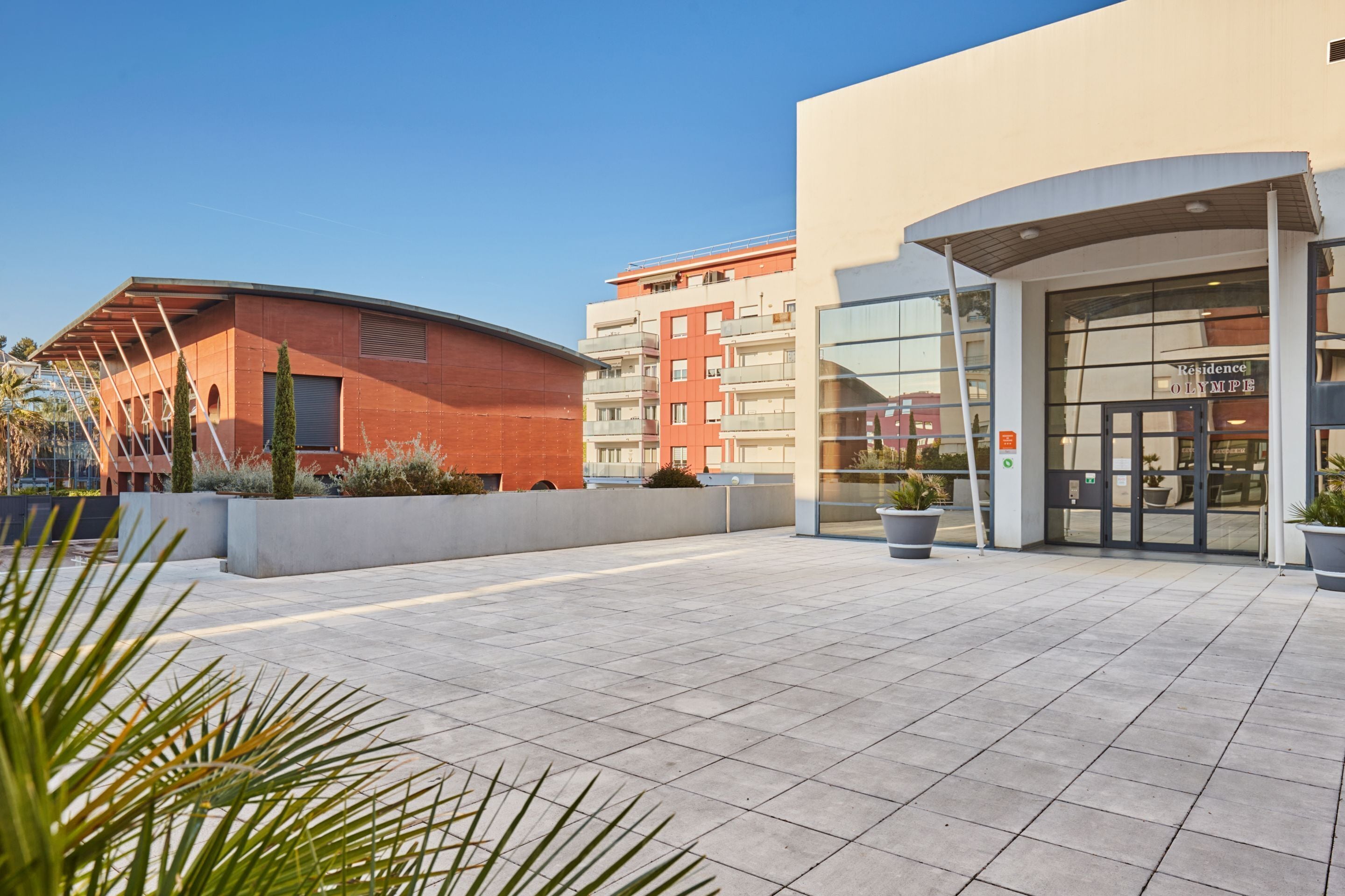 Un edificio moderno con fachada curva, entrada de vidrio y patio empedrado.