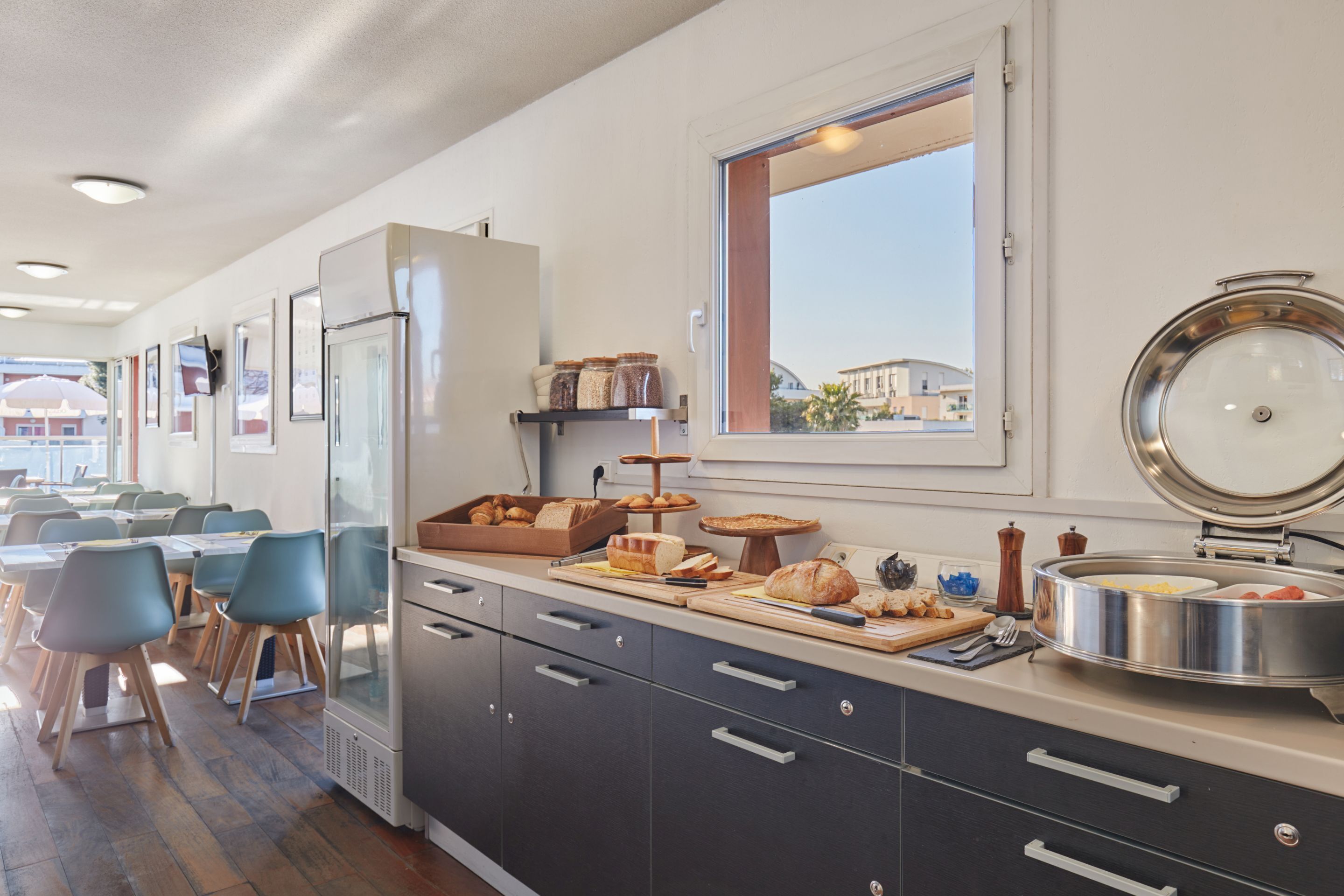 Eine moderne Küche mit Essbereich, ausgestattet mit einem großen Fenster, Edelstahlgeräten und verschiedenen Lebensmitteln auf der Arbeitsfläche.