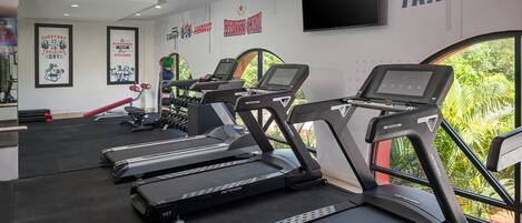 Un gimnasio con cintas de correr, equipo de ejercicio, carteles motivacionales y una pantalla de televisión.
