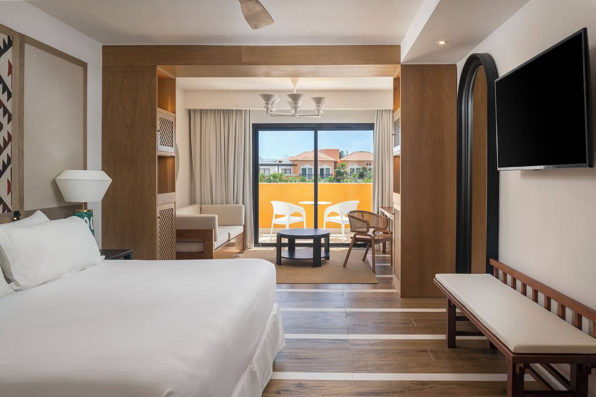 Une chambre d’hôtel dotée d’un grand lit, d’une télévision, d’un balcon avec vue et d’un coin salon avec une table et des chaises.
