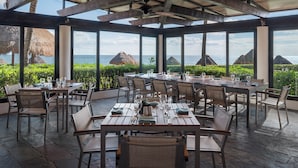 A covered outdoor dining area with tables set for two, overlooking the sea.