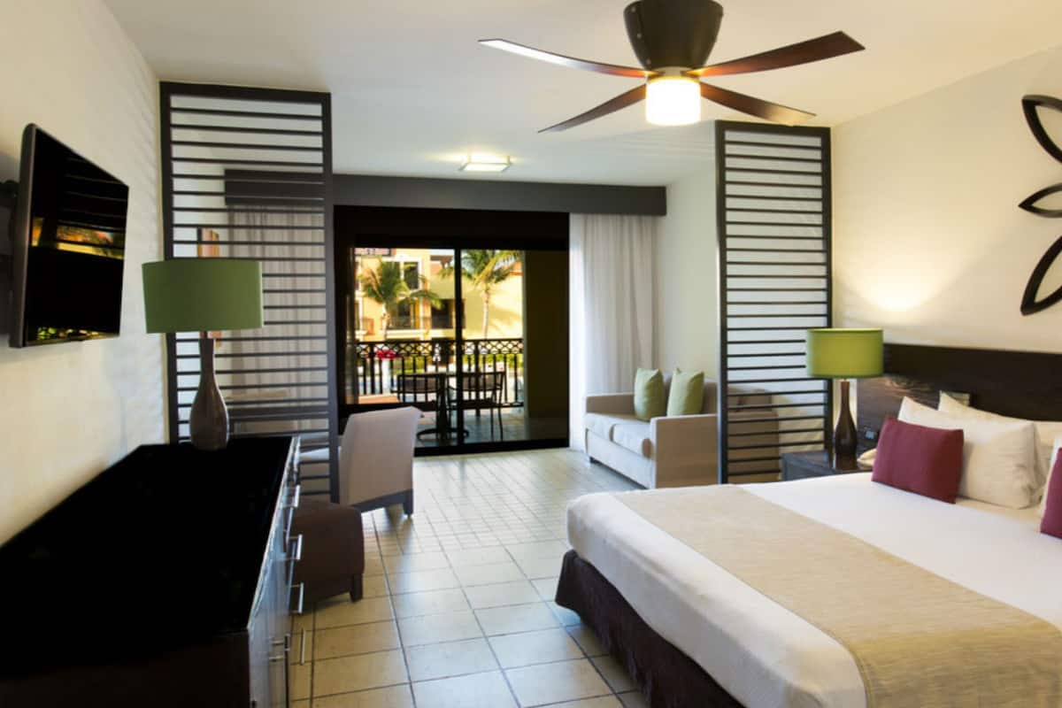 Une chambre d’hôtel équipée d’un lit, d’un bureau, d’une chaise, d’un balcon avec vue et d’un ventilateur de plafond.