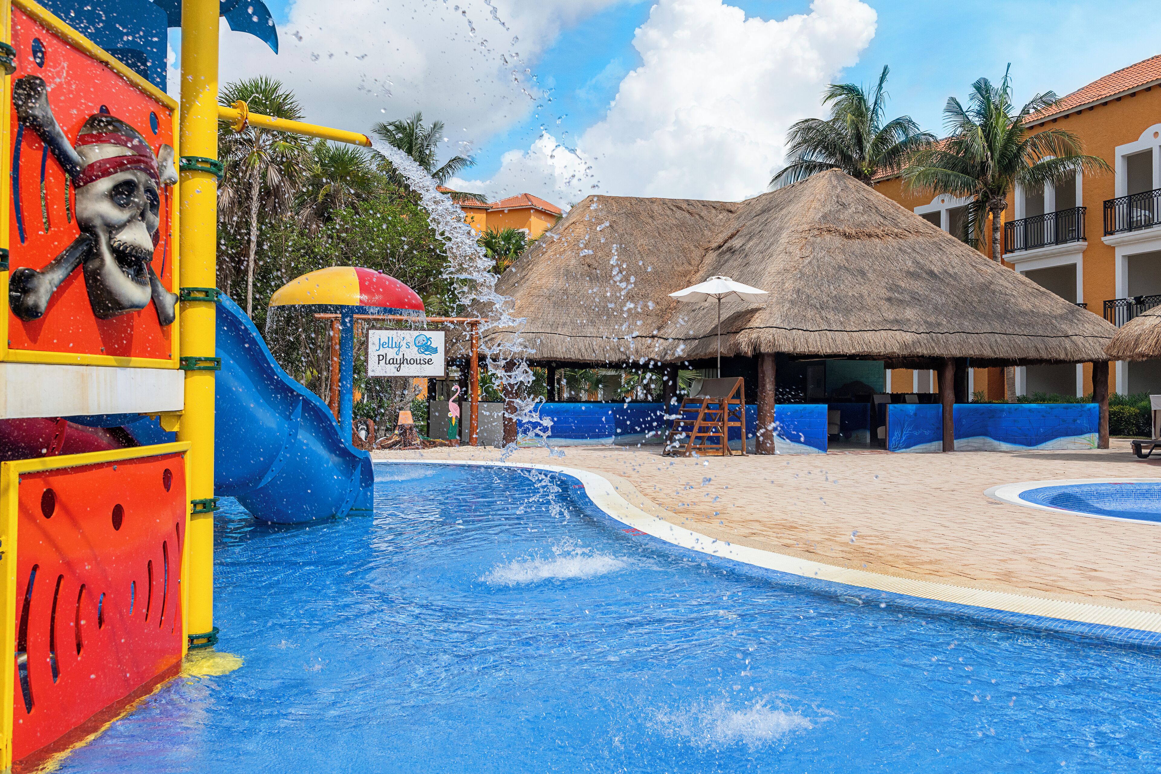 A water park area with a blue pool, a pirate-themed slide, and thatched-roof structures.