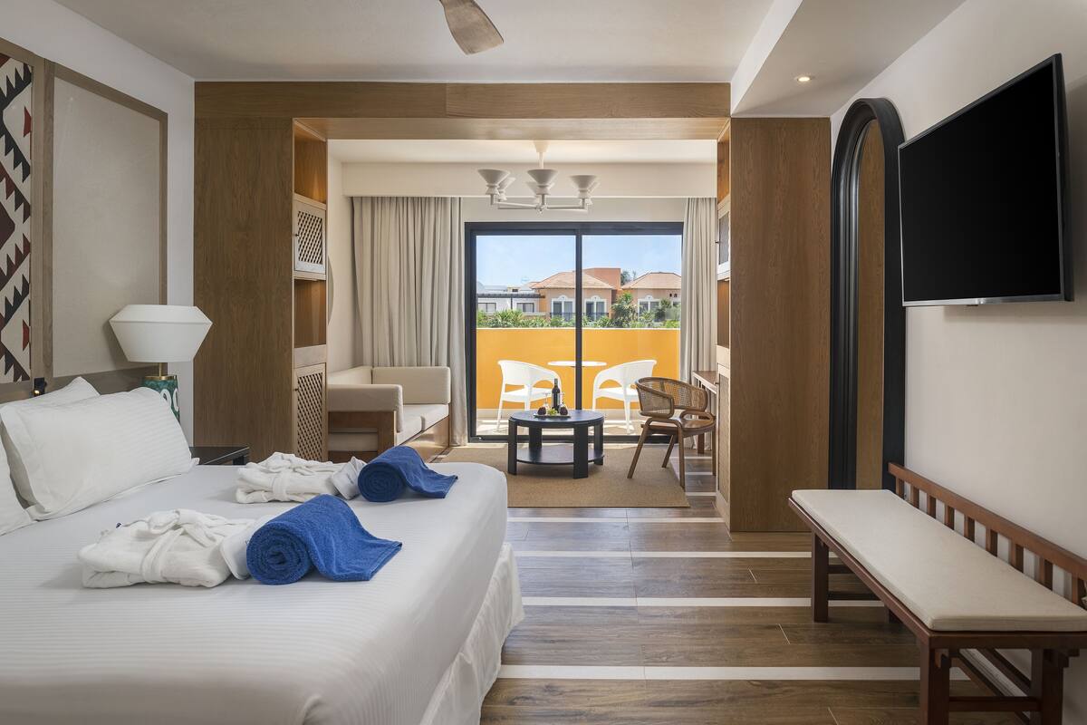 Une chambre d’hôtel comprenant un lit, un banc, une télévision, un balcon avec vue et un coin repas.