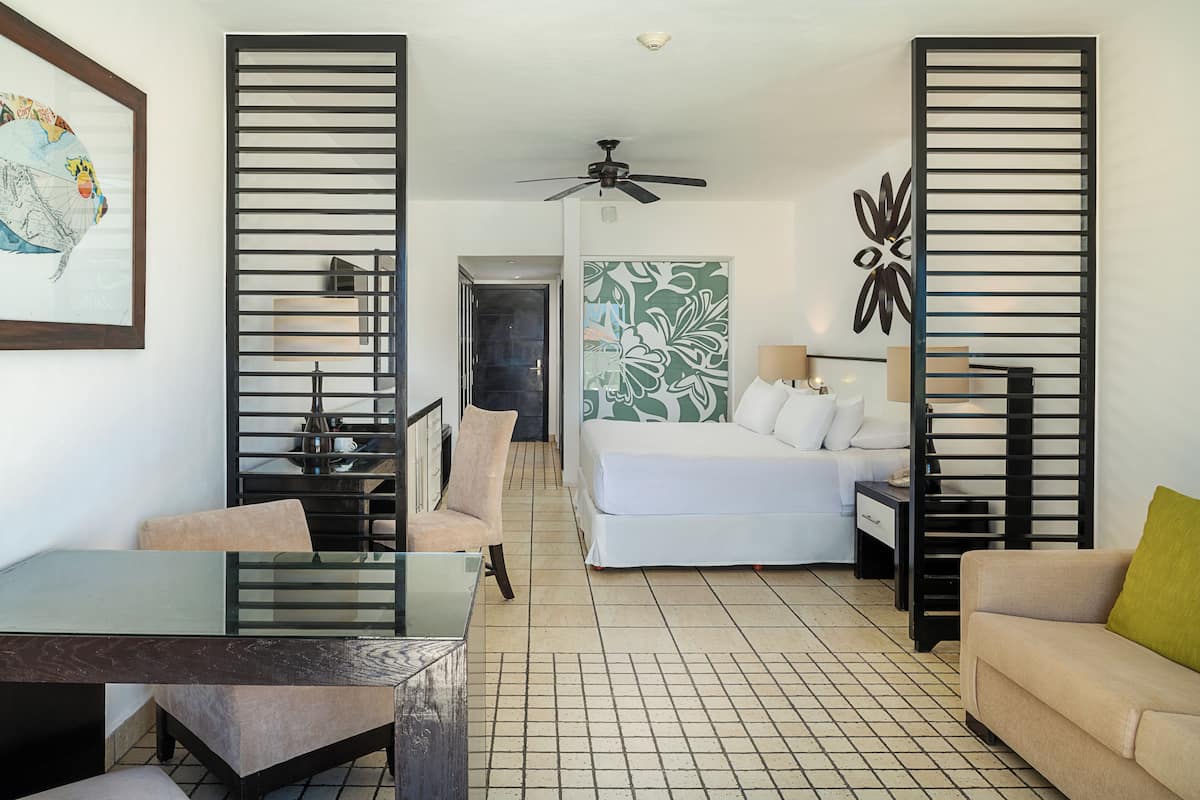 Une chambre d’hôtel comprenant un lit, un bureau, une chaise, un canapé, un ventilateur de plafond et un élément décoratif mural.