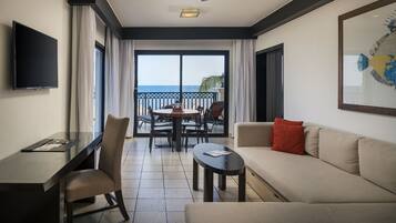 A hotel room with a balcony, a dining table, a sofa, a TV, and a ceiling fan.