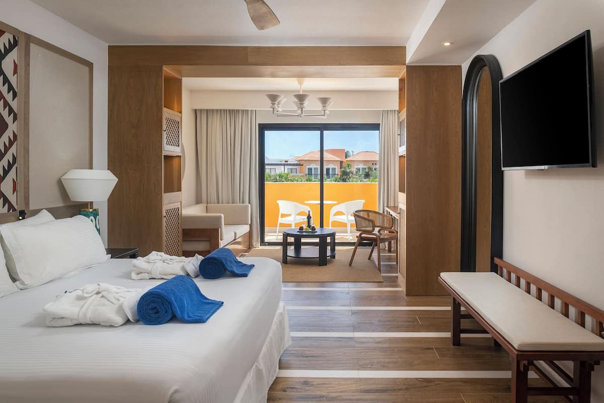 Habitación de hotel con cama, televisión, balcón con vistas y zona de estar.