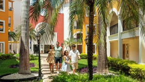 A courtyard with a pathway, palm trees, and buildings with balconies. - Ocean Coral & Turquesa All Inclusive (Puerto Morelos)