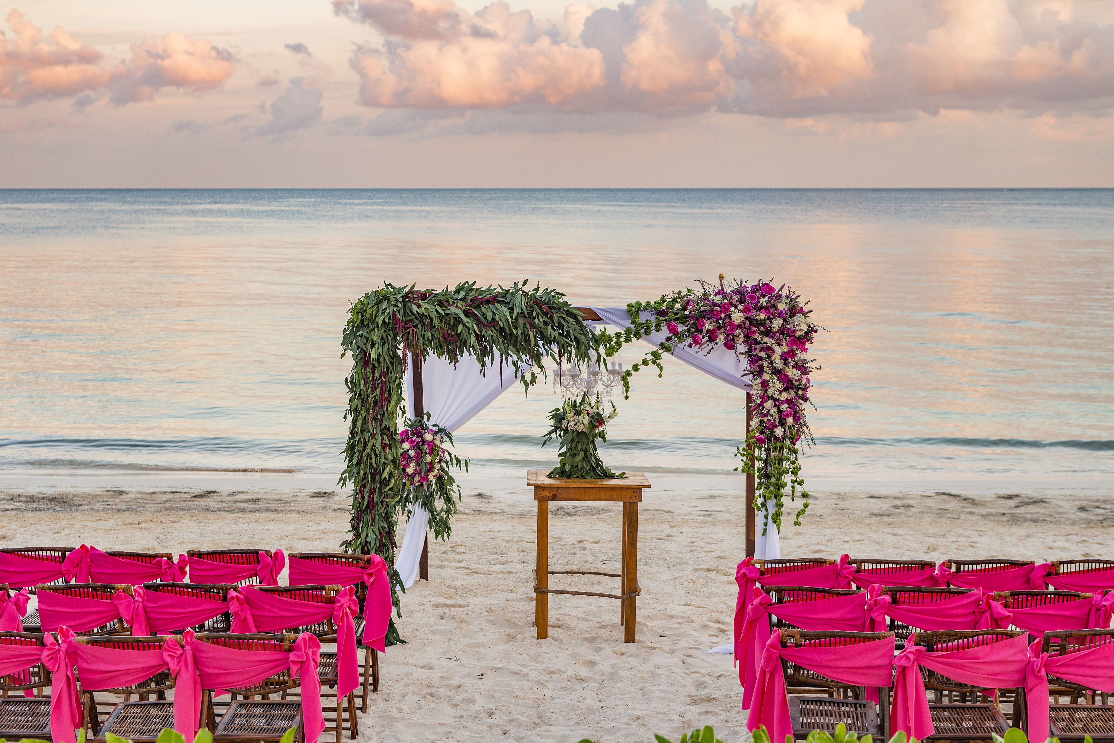 Decoración de boda en la playa con sillas de madera y un arco floral.