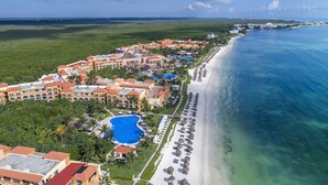 An aerial view of a resort with a beachfront, a swimming pool, and multiple buildings with red roofs.