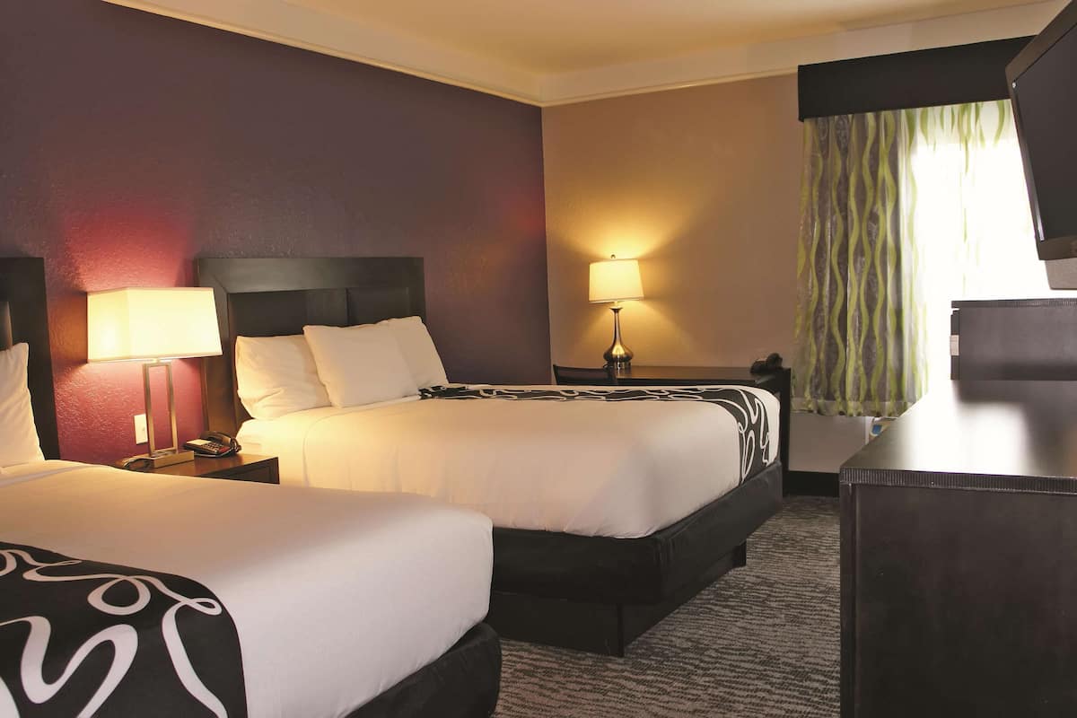 A hotel room with two beds, a desk, and a TV.