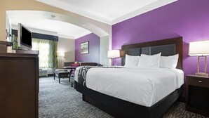 Ein Hotelzimmer mit einem großen Bett, einem Schreibtisch, einem Sessel, einem Fernseher und einer Lampe.