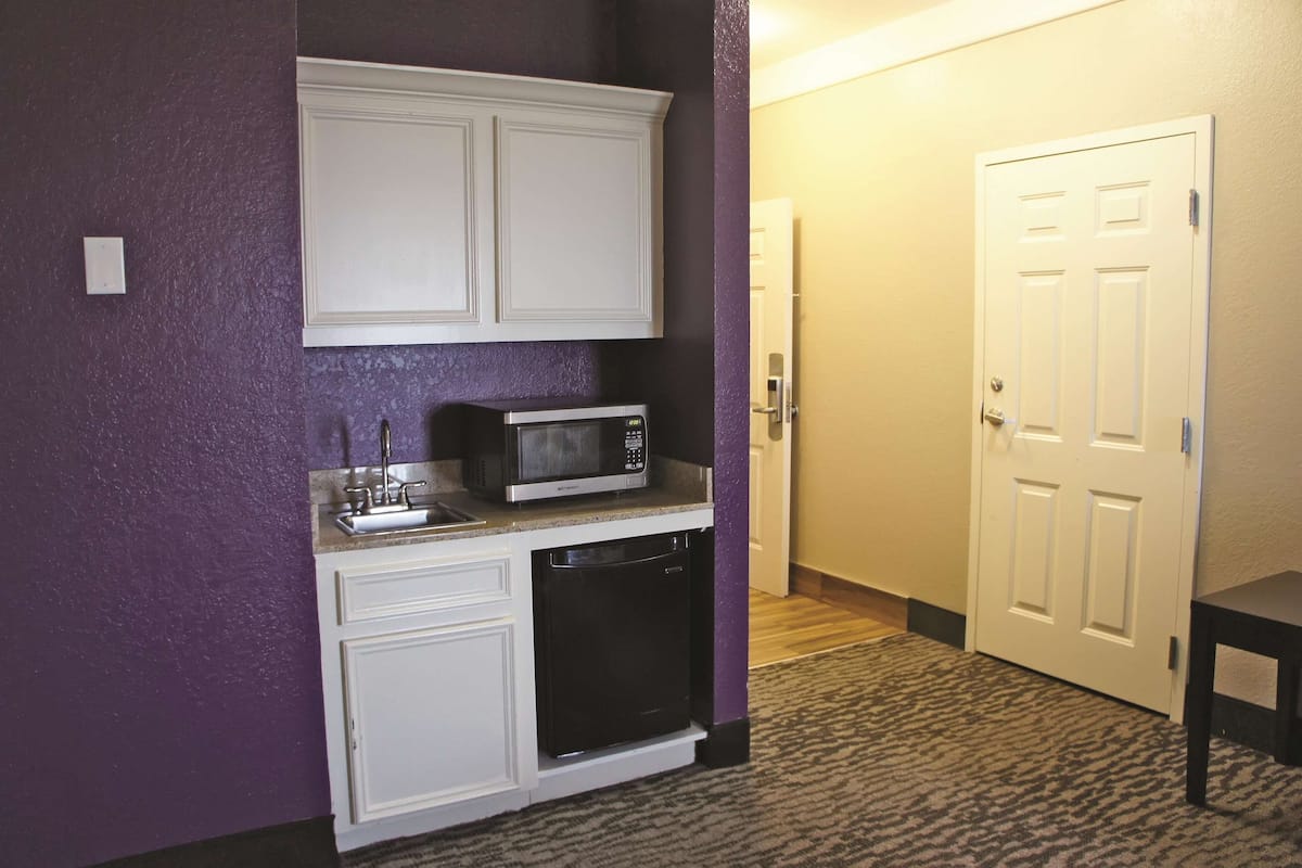 A compact kitchenette with a microwave, sink, and dishwasher, adjacent to a door and a small table.