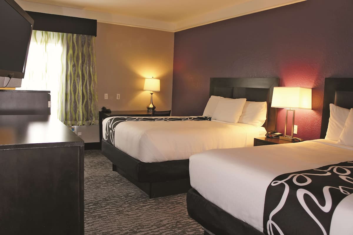 A hotel room with two beds, a desk, and a lamp.