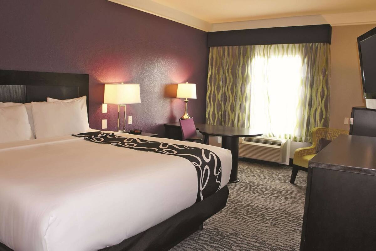 A hotel room with a large bed, two bedside lamps, a desk with a chair, and a television.