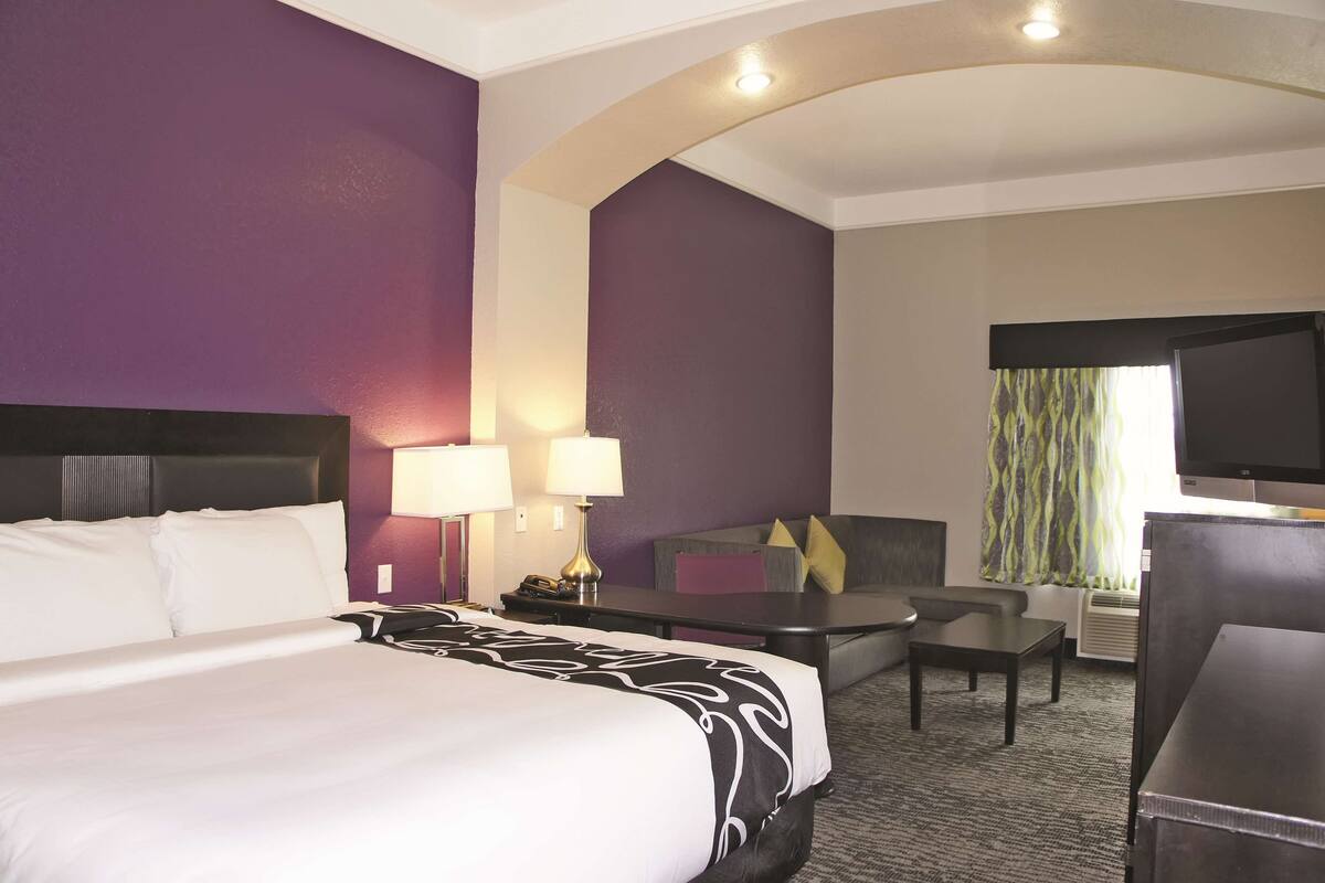 A hotel room with a bed, a desk, a chair, a television, and a window with curtains.