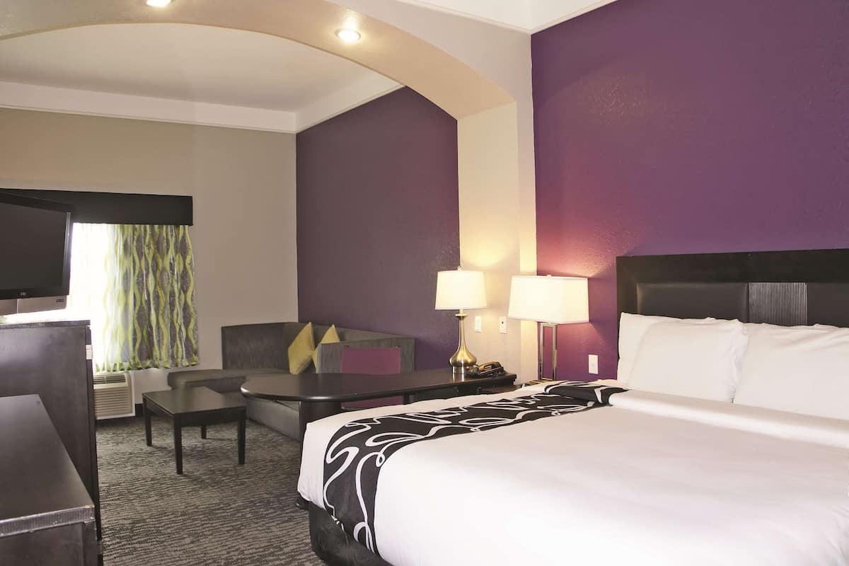 A hotel room with a bed, a desk, a chair, a TV, and a lamp.