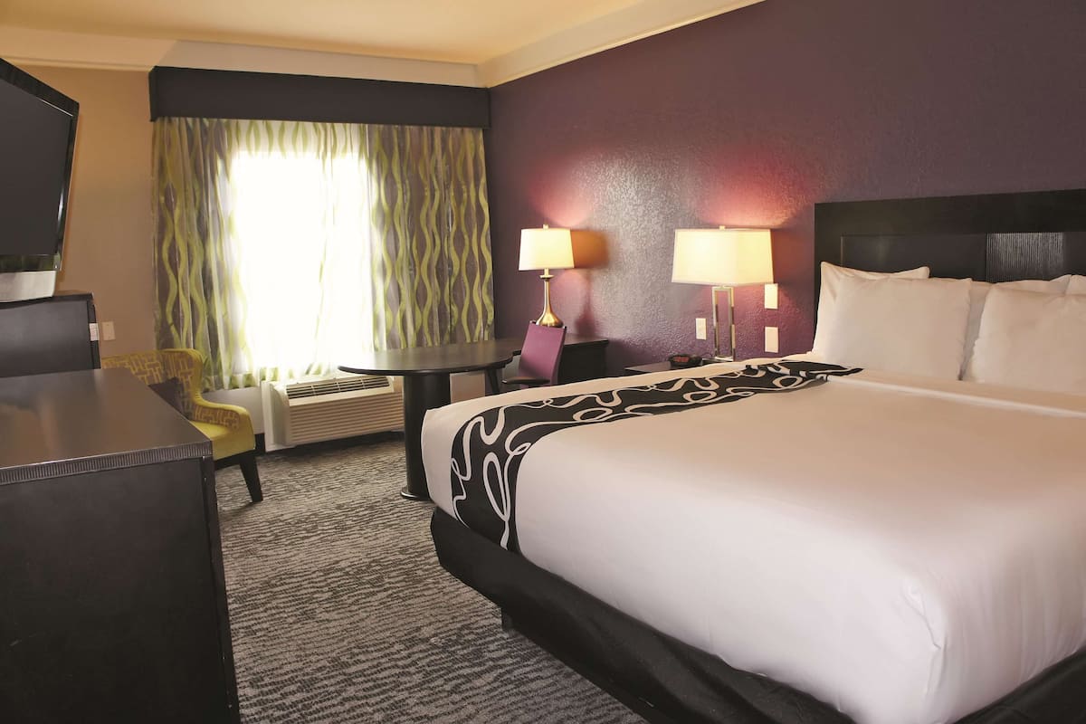 A hotel room with a large bed, two bedside lamps, a desk, a chair, and a window with curtains.