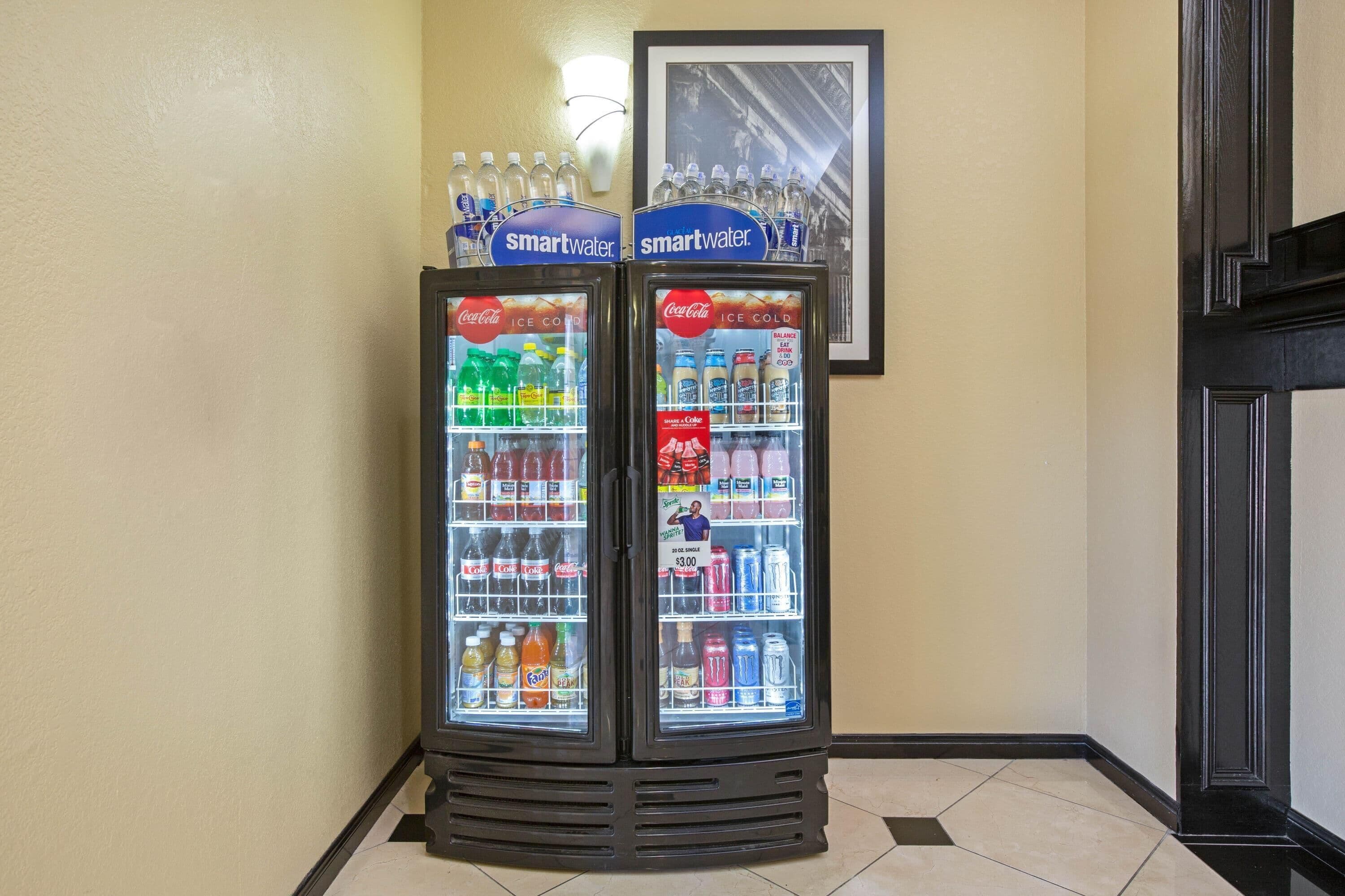 A vending machine with 'smartwater' and 'Coca-Cola' branded bottles, and a framed picture on the wall.