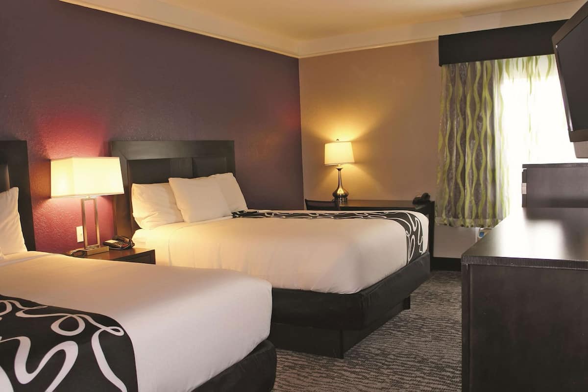 A hotel room with two beds, a desk, a lamp, and a television.