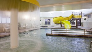 Een binnenzwembad met een gele glijbaan, witte stoelen en een jacuzzi.